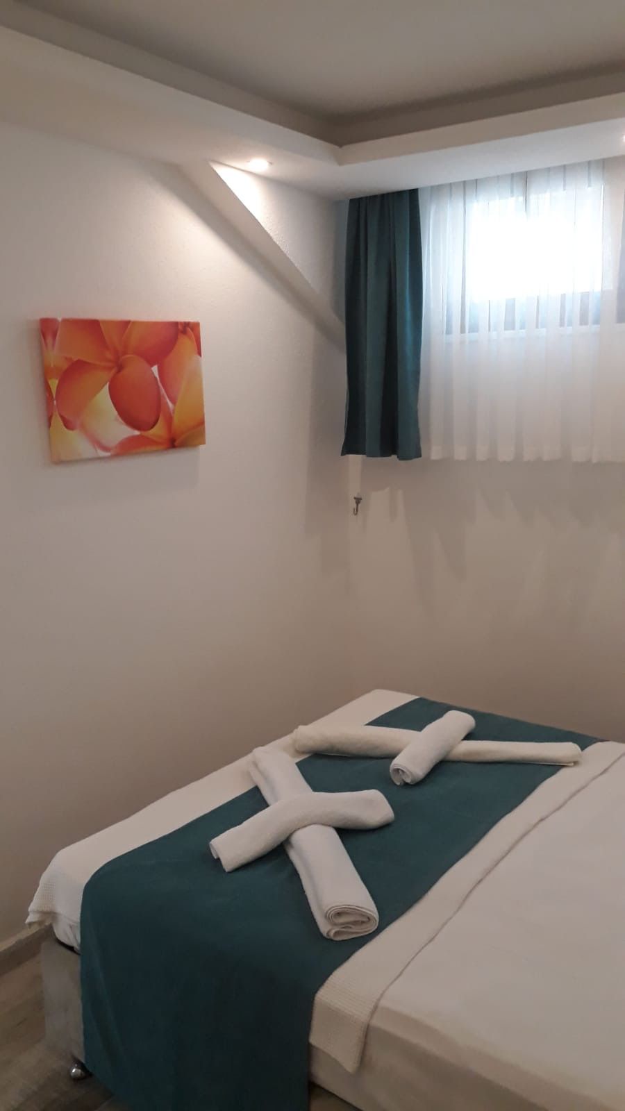 A hotel room with a bed, a painting on the wall, a window with curtains, and a towel on the bed.