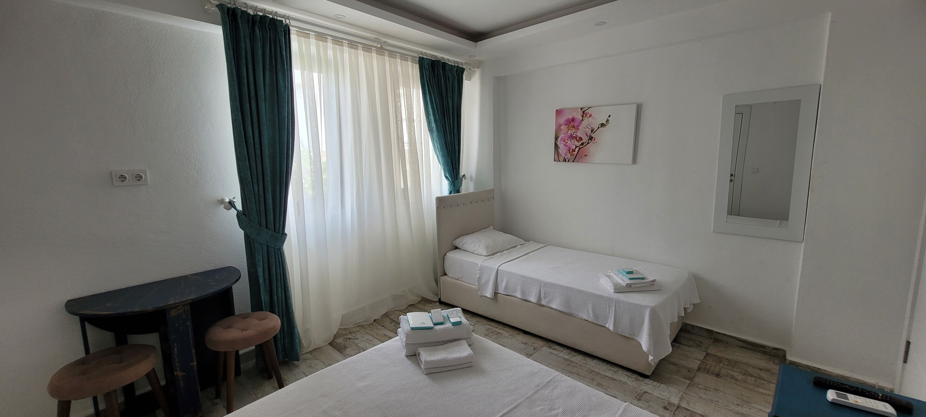 A small, neatly arranged bedroom with a single bed, a bedside table, a chair, and a window with curtains.