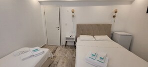 A hotel room with a bed, a bedside table, a wardrobe, and a small desk. - Tenes Otel (Bozcaada)
