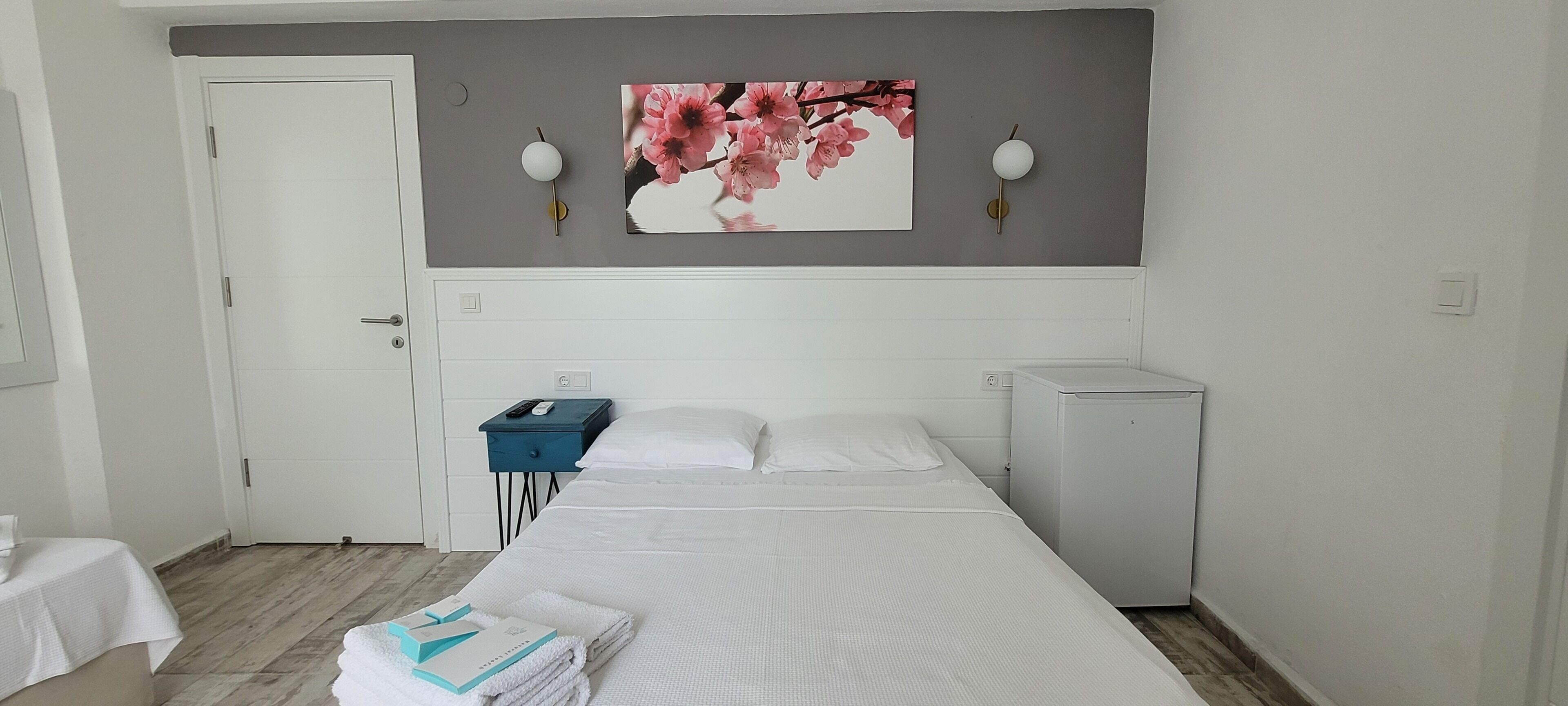 Hotellihuone, jossa on sänky, työpöytä, tuoli, pieni pöytä, yöpöytä, seinään kiinnitetty lamppu ja taulu.