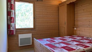 En stuga med träpanel, ett rum med en säng, ett fönster med gardiner och en inbyggd värmare.