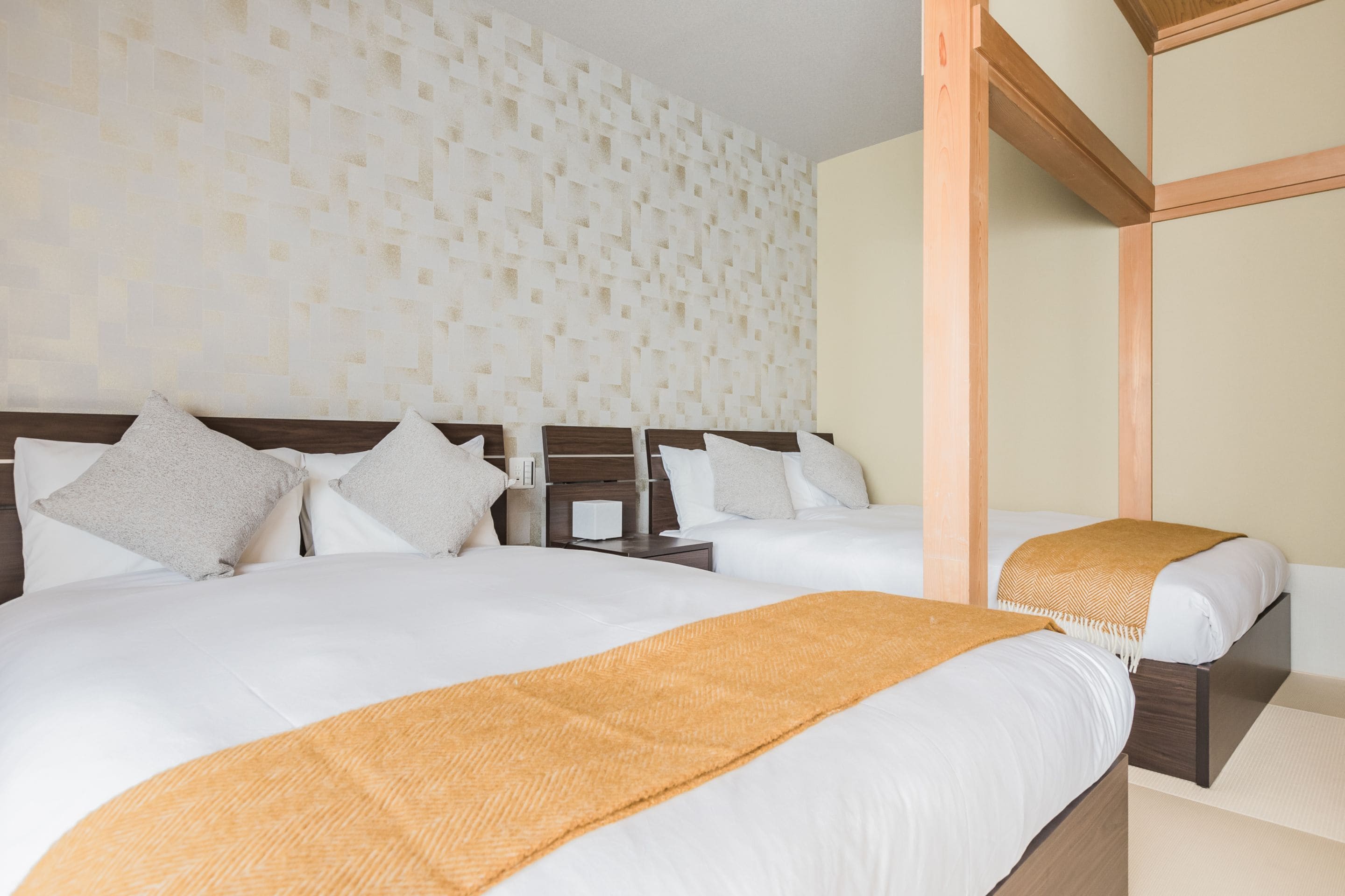 A hotel room with two beds, a wooden headboard, a textured wall, and a nightstand with a lamp.