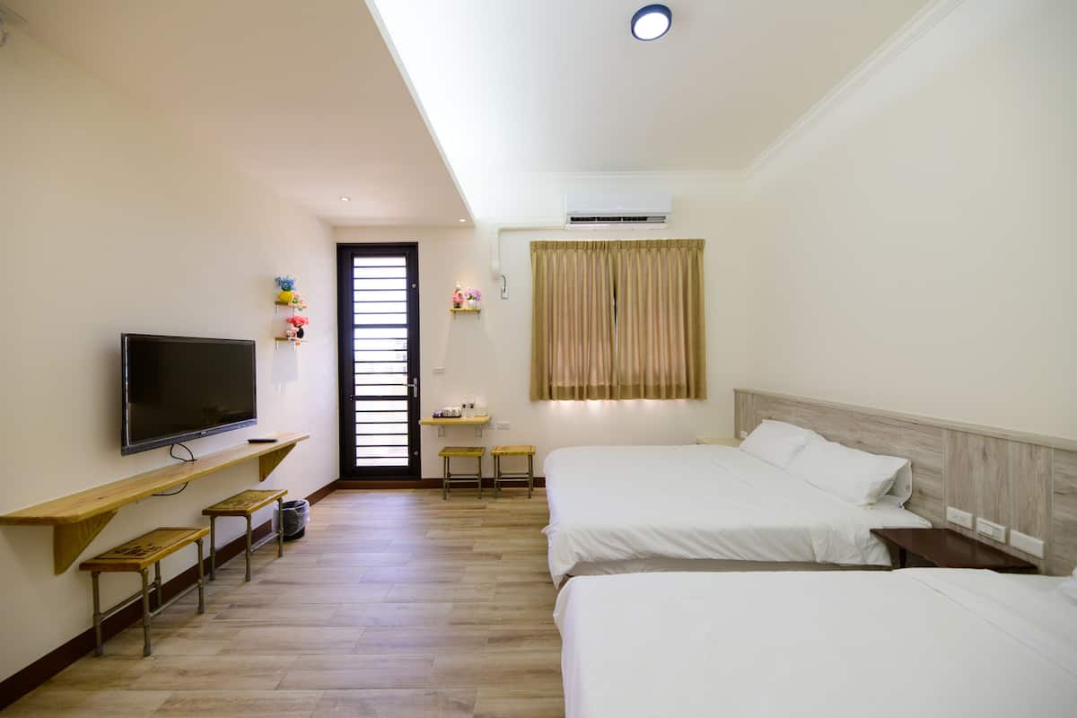 A hotel room with two beds, a TV, a small desk, and a window with curtains.