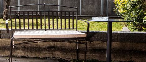 A metal bench with a cushion, positioned next to a small round table with a newspaper.