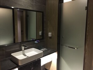 A modern bathroom with a rectangular sink, a mirror, and a frosted glass door.