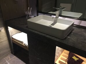 Un baño moderno con un lavamanos blanco, encimera de mármol oscuro y mueble de tocador de madera.