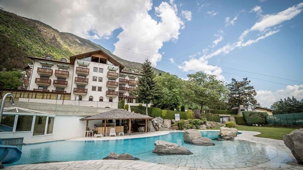 A hotel with a pool, outdoor seating, and a mountainous backdrop. - Hotel Vermoi (Laces)