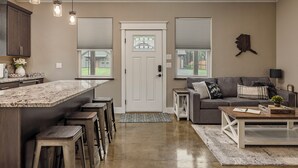 Una cocina moderna con encimera de mármol y taburetes de bar, un área de estar con sofá y mesa de centro, y una puerta con un vitral.