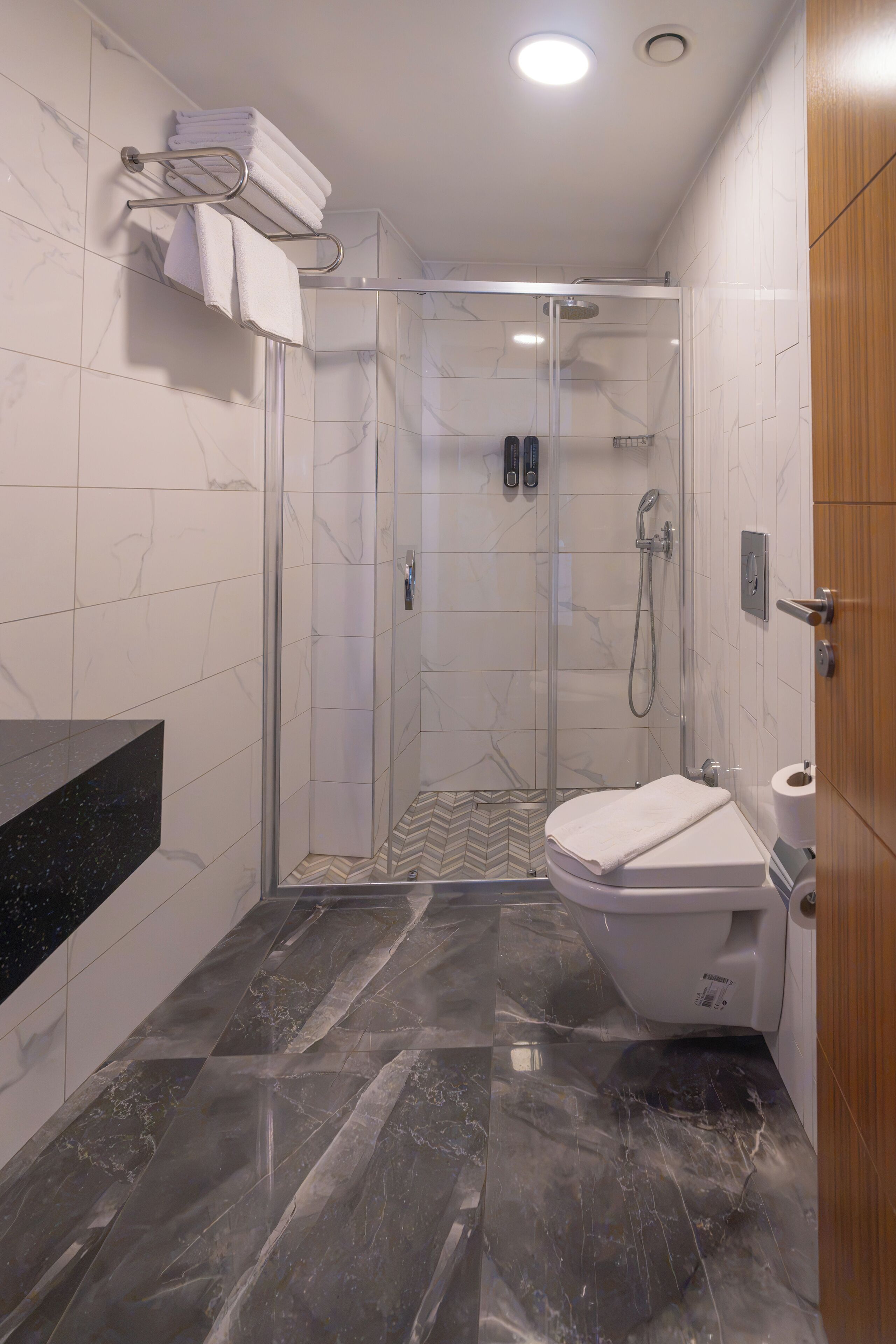 Un baño moderno con ducha de vidrio, inodoro y tocador con encimera negra.