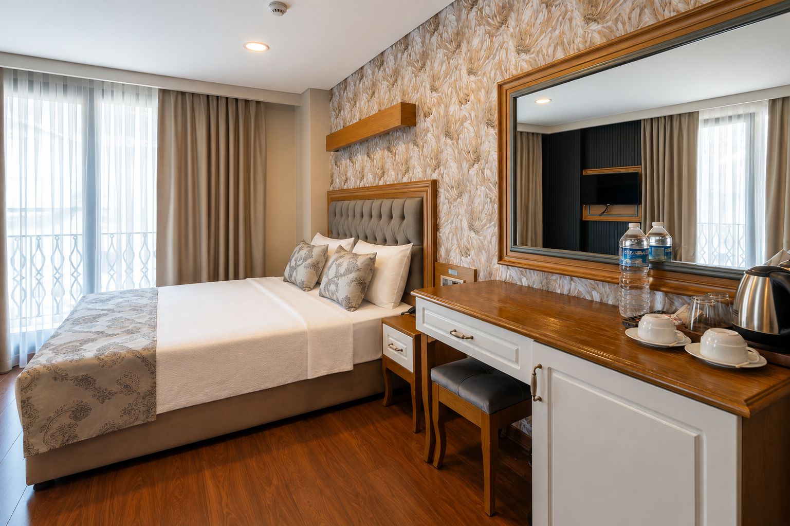 Une chambre d’hôtel avec un lit, un bureau, une chaise, un miroir et une fenêtre avec des rideaux.