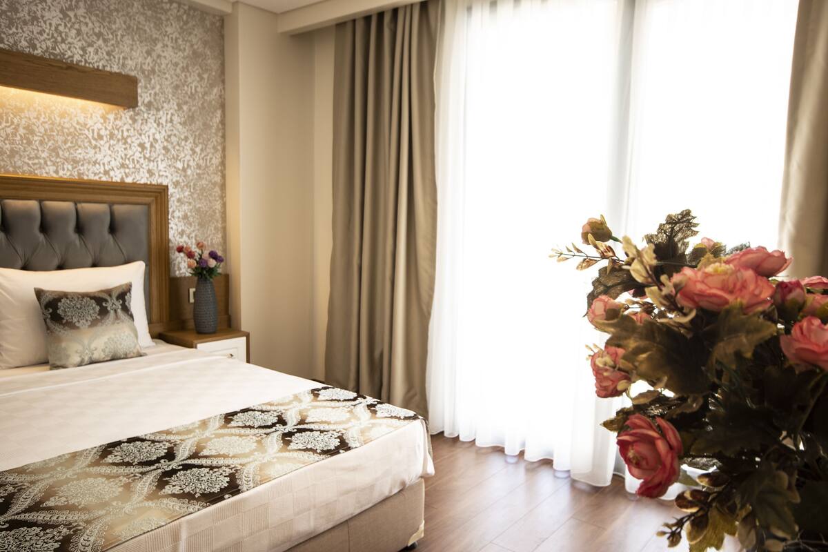 Ein Hotelzimmer mit Bett, Vorhängen und einer großen Blumenkomposition.