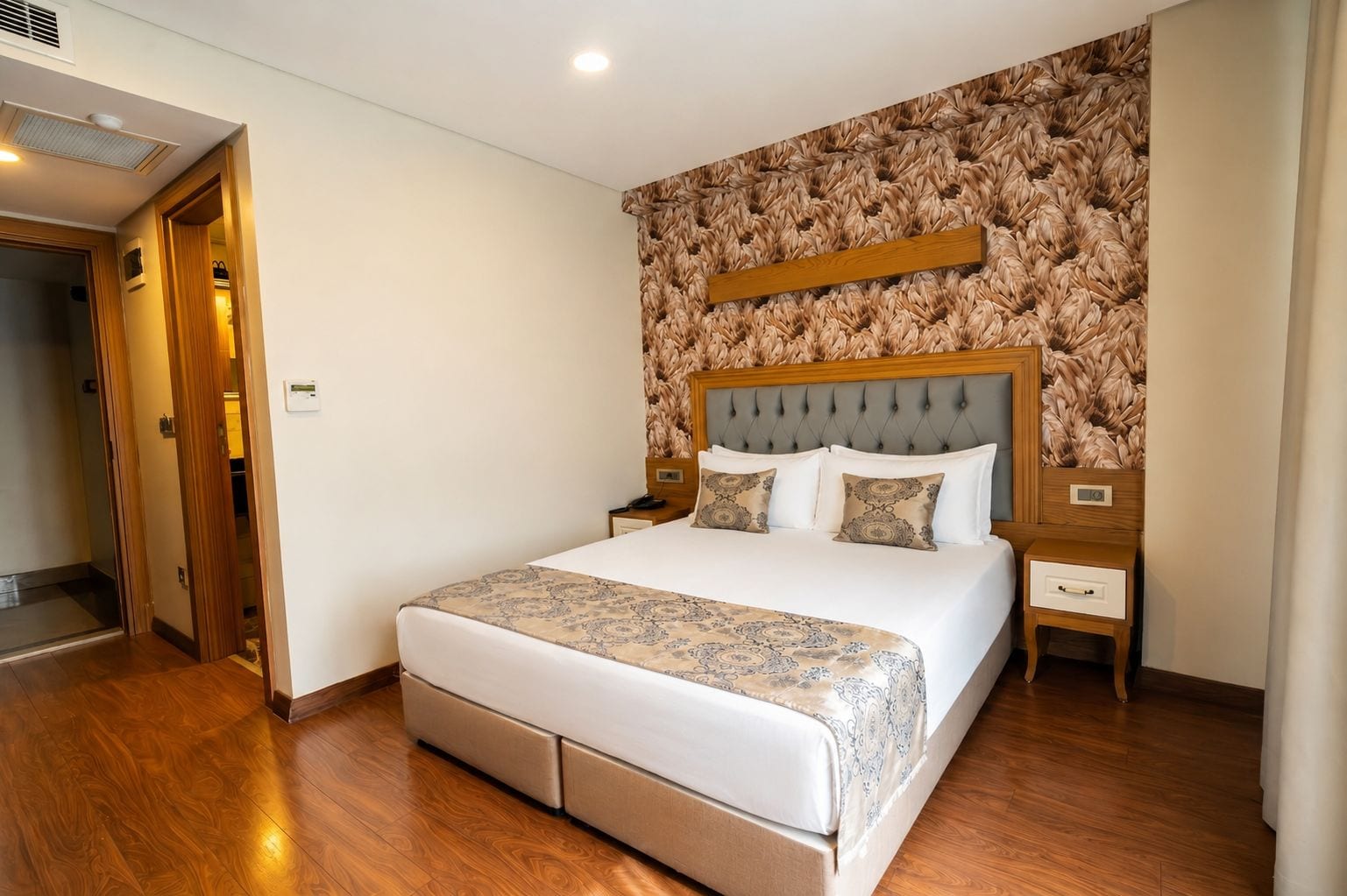 Une chambre d’hôtel avec un grand lit, une tête de lit en bois et un mur décoré d’un motif.