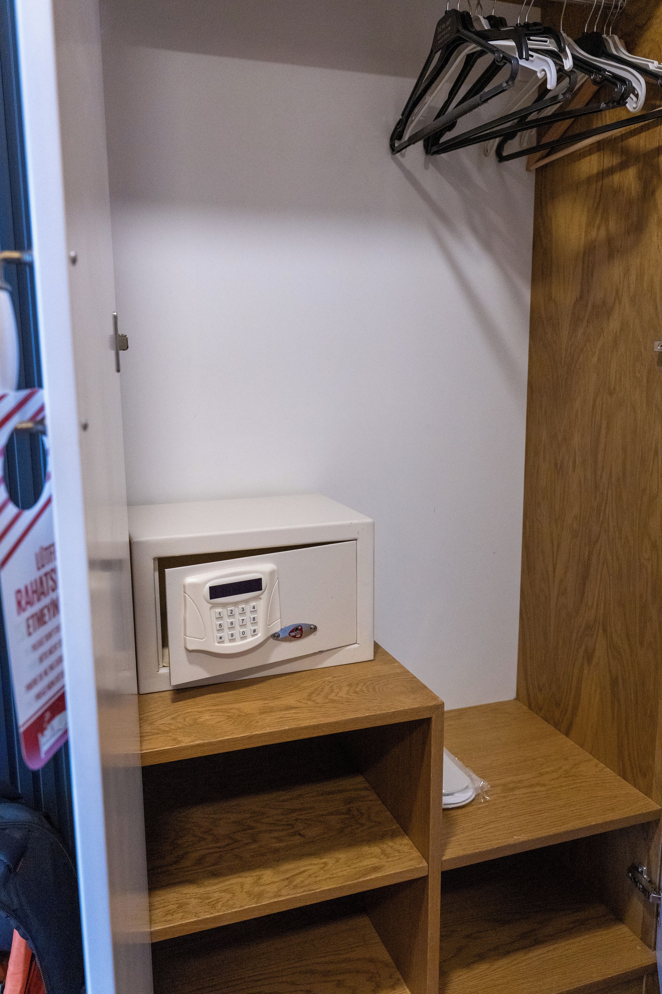 A white microwave on a wooden shelf in a room with a wooden door and a coat rack with hangers.