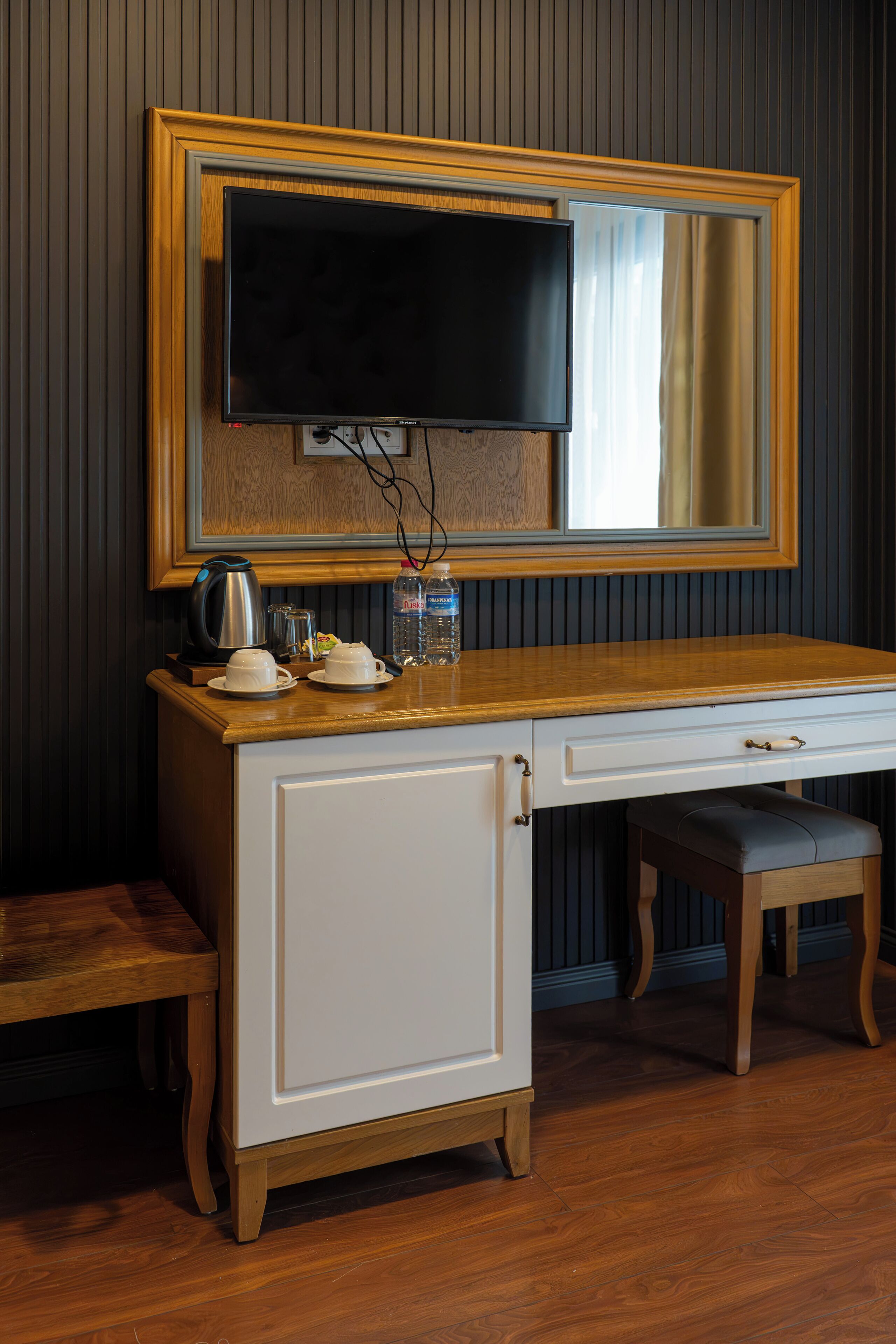 A room with a wooden desk, a television mounted on the wall, a cabinet, and a bench.