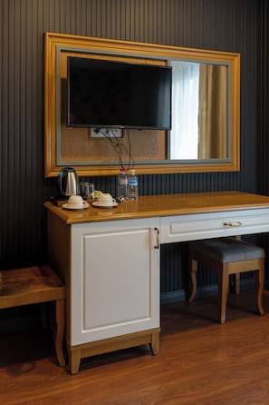 Una habitación con un escritorio de madera, un televisor montado en la pared, un armario y un banco.