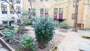 A courtyard with a large bush, a bench, and a building with multiple windows and a brick facade. - Modern 2 bed flat in historic building (London)