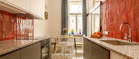 Una cocina con salpicadero de azulejos, una ventana con cortinas y un comedor con sillas y mesa.