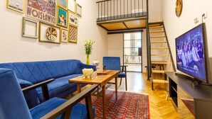 A living room with a blue sofa, a wooden coffee table, and a TV on a stand. - Das Hostel (Kraków)