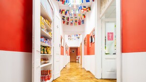 A hallway with shelves stocked with snacks and beverages, a wooden herringbone floor, and a door at the end. Flags are hanging from the ceiling. - Das Hostel (Kraków)