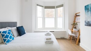 Una camera d'albergo moderna con un letto grande, una finestra a bovinda, una scrivania con una sedia e un quadro appeso al muro.