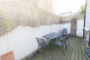 A patio area with a table and chairs, a white wall, and a brick wall.