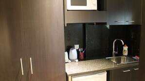 Een kleine keuken met donkerhouten kastjes, een roestvrijstalen spoelbak, een magnetron en een koffiezetapparaat.