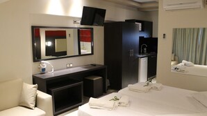 Een hotelkamer met een bed, een bureau met stoel, een spiegel, een televisie, een kledingkast en een kleine kitchenette.