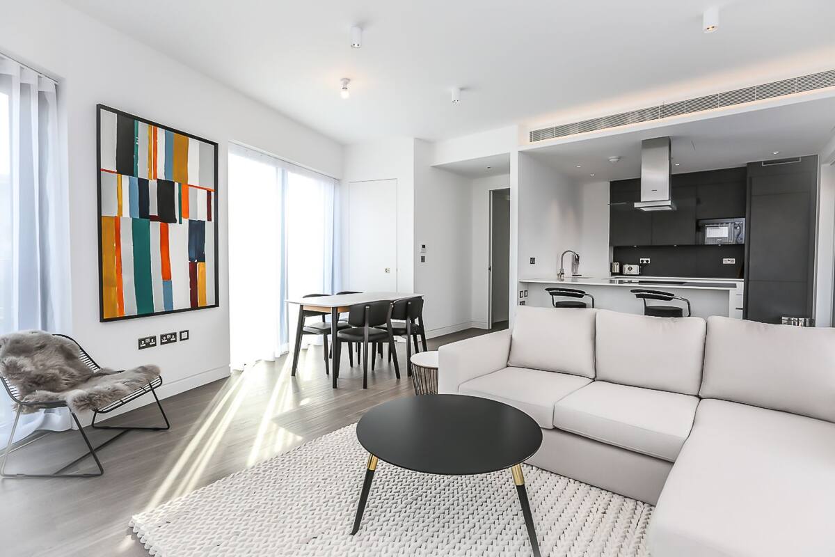 A modern living room with a white sofa, a dining table with chairs, a black coffee table, and a colorful abstract painting on the wall.