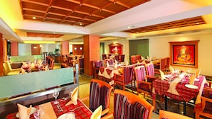 A restaurant with multiple dining tables and chairs, wooden ceiling, and a large painting on the wall. - The Classik Fort (Kanayannur)