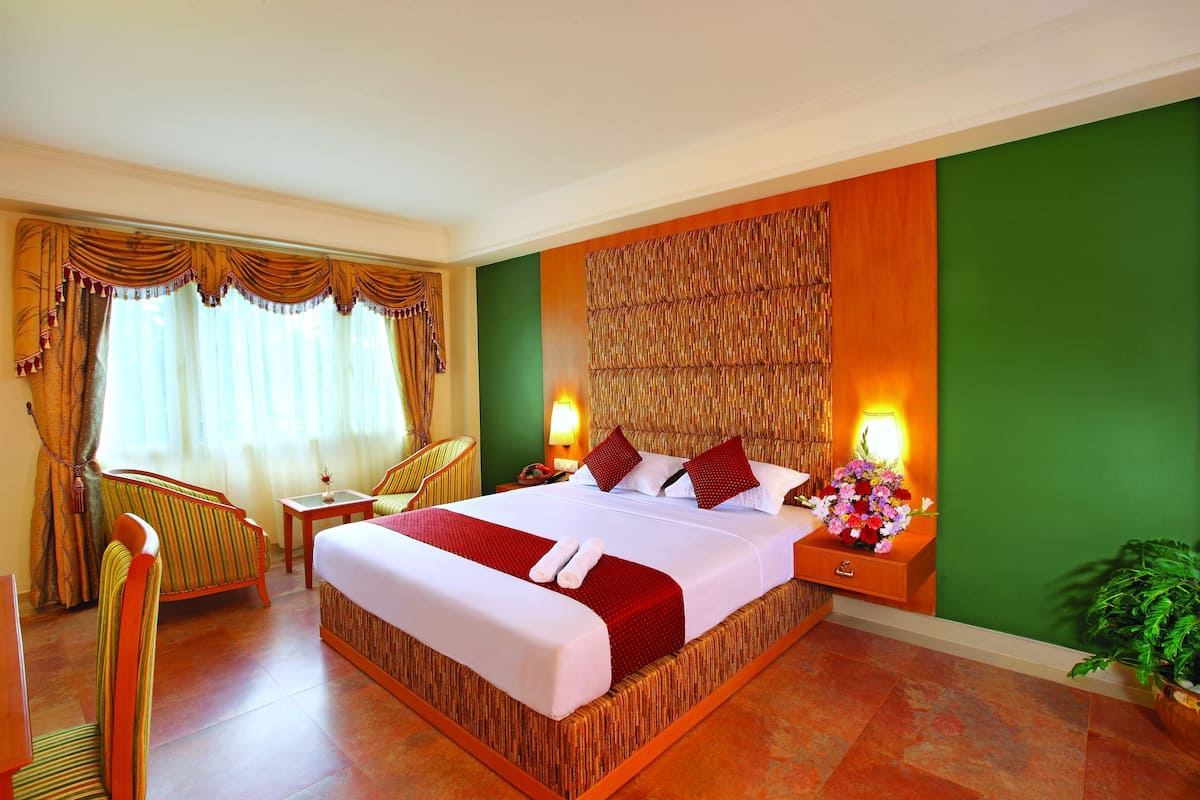 A hotel room with a large bed, two bedside tables with lamps, a chair, and a potted plant.