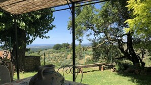 A rustic outdoor seating area with a table, a ceramic pot, and a view of a hilly landscape. - Hous Malerin with sea view, fenced garden - by ToscanaTour (Guardistallo)