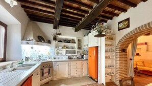 A kitchen with white cabinets, an orange refrigerator, and a brick wall. - Hous Malerin with sea view, fenced garden - by ToscanaTour (Guardistallo)