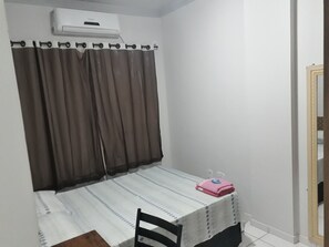 A small room with a bed, a chair, a table with a pink item on it, and a window with curtains.