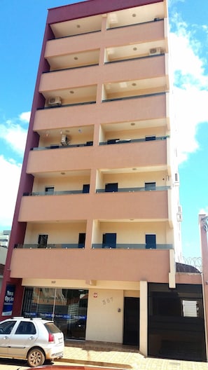 A multi-story building with balconies, a car parked in front, and a visible storefront with signage.