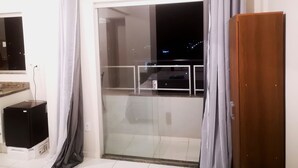 A room with a sliding glass door leading to a balcony, an air conditioning unit mounted above the door, a small black speaker on the floor, and a wooden door to the right. - Unai ApartFlat (Unai)