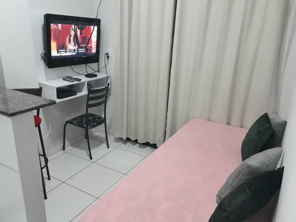 Ett litet rum med en säng, ett skrivbord med en dator och en tv.