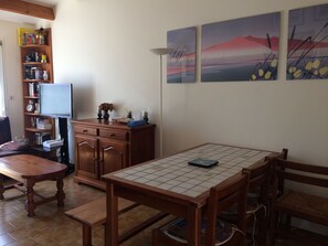 A cozy living room with a wooden coffee table, a TV, a bookshelf, and a dining table with chairs.