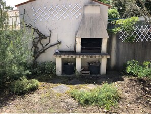 A concrete outdoor kitchen with a chimney, two trash bins, and a white lattice fence.