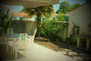 Une terrasse avec une table et des chaises, un palmier et un espace barbecue.