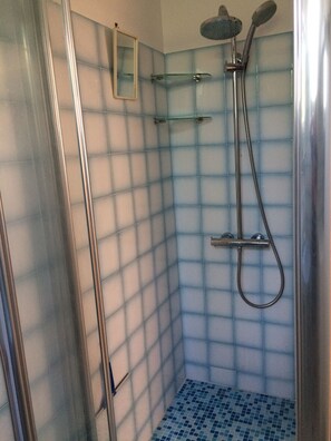 Une douche avec une porte en verre, un pommeau de douche à main et un robinet mural.