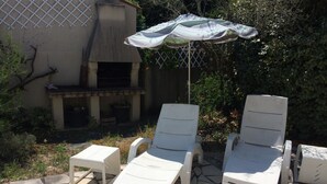En terrasse med to hvide liggestole, et lille bord, en parasol og en gulv belagt med sten.