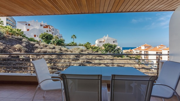A terrace with a table and chairs, overlooking a hillside with buildings and a clear sky. - Balcon de Los Gigantes 2A037 (Acantilados de Los Gigantes)