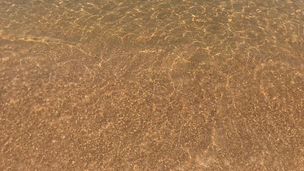 On aperçoit clairement une plage avec une eau calme, un bateau et des bouées flottantes.