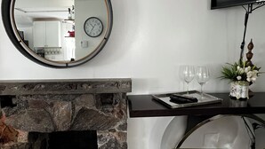 Un salon moderne doté d’une cheminée en pierre, d’un miroir rond, d’un téléviseur à écran plat et d’un coin repas avec une table et des chaises.