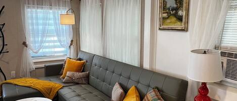 A living room with a grey sofa, a round coffee table, a red lamp, and a painting on the wall.