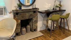 Un salon moderne avec une cheminée en pierre, un miroir rond, un téléviseur à écran plat, un coin repas avec deux chaises et un plancher en bois.