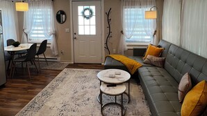 Un salon comprenant un canapé, une table basse, un coin repas avec des chaises, un lustre et une porte ornée d’une guirlande.