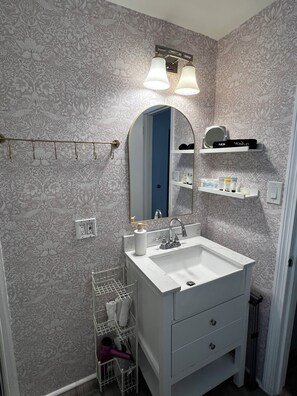 A bathroom with a white sink, a mirror, a towel rack, and a shelf with toiletries. - COZY,Newly renovated,West Shores ,short walk to Nasons Beach 🏖🏠 (Sebago)