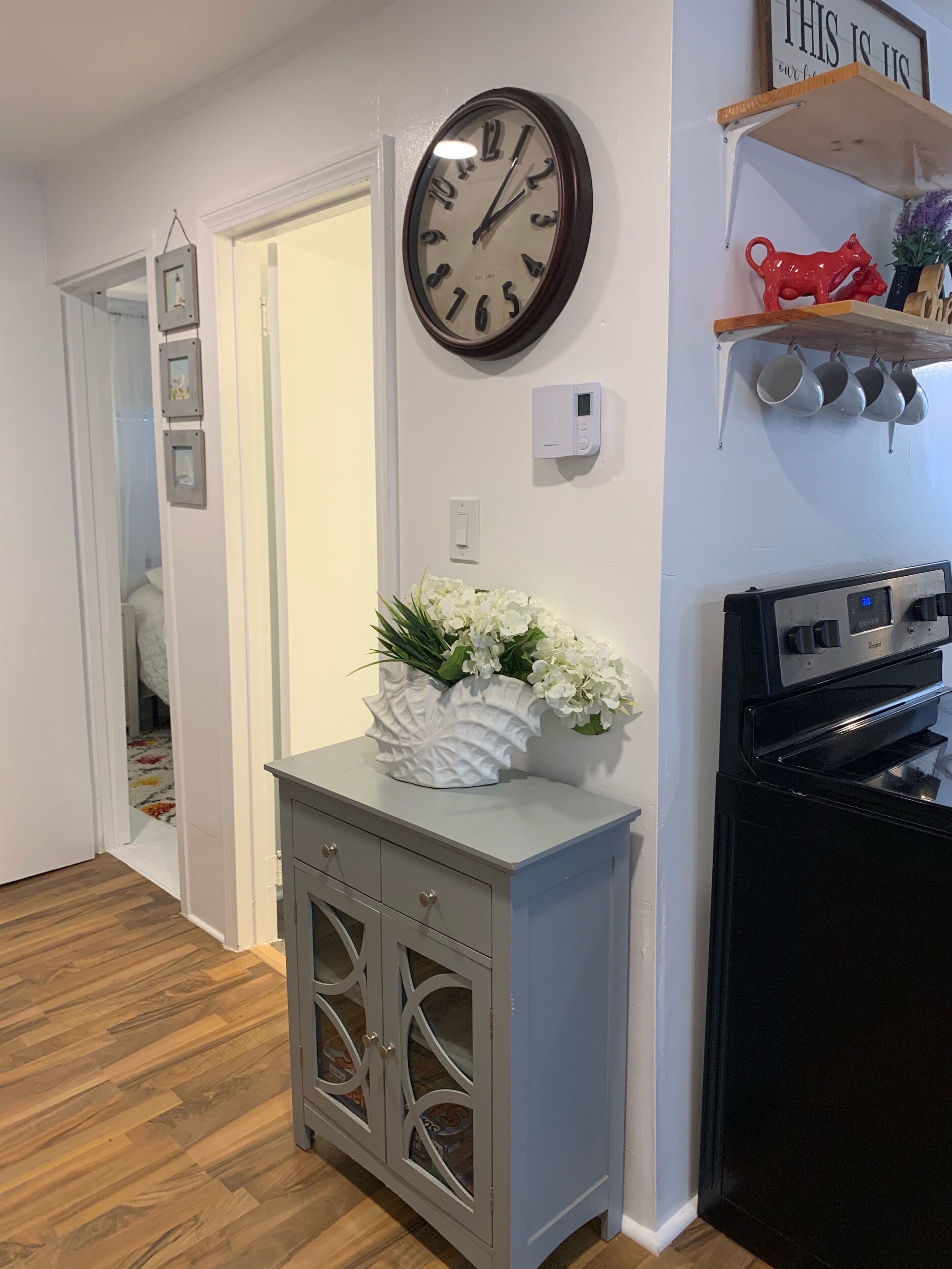 A kitchen with a clock, a stove, and a cabinet with drawers.