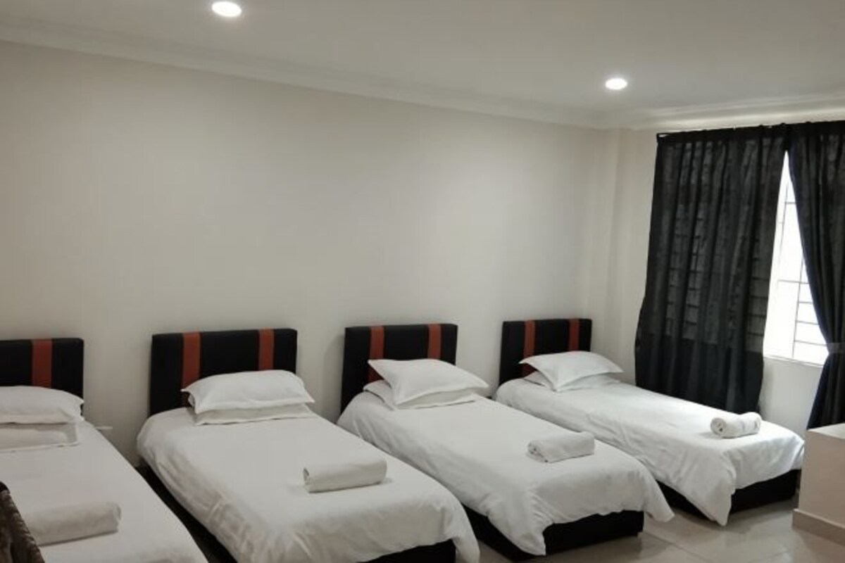 A hotel room with four single beds, a window with curtains, and a white wall.
